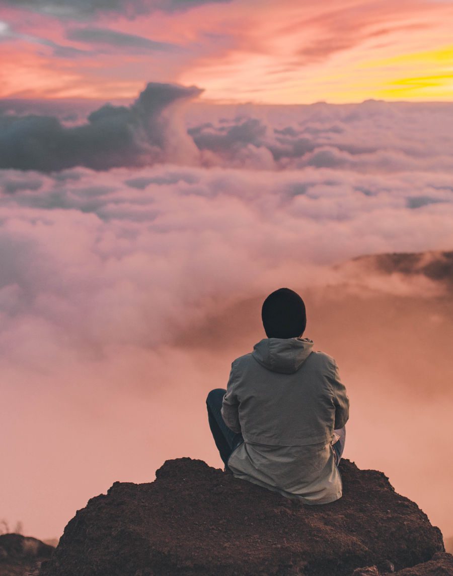 person sitting on top of mountain looking at clouds below